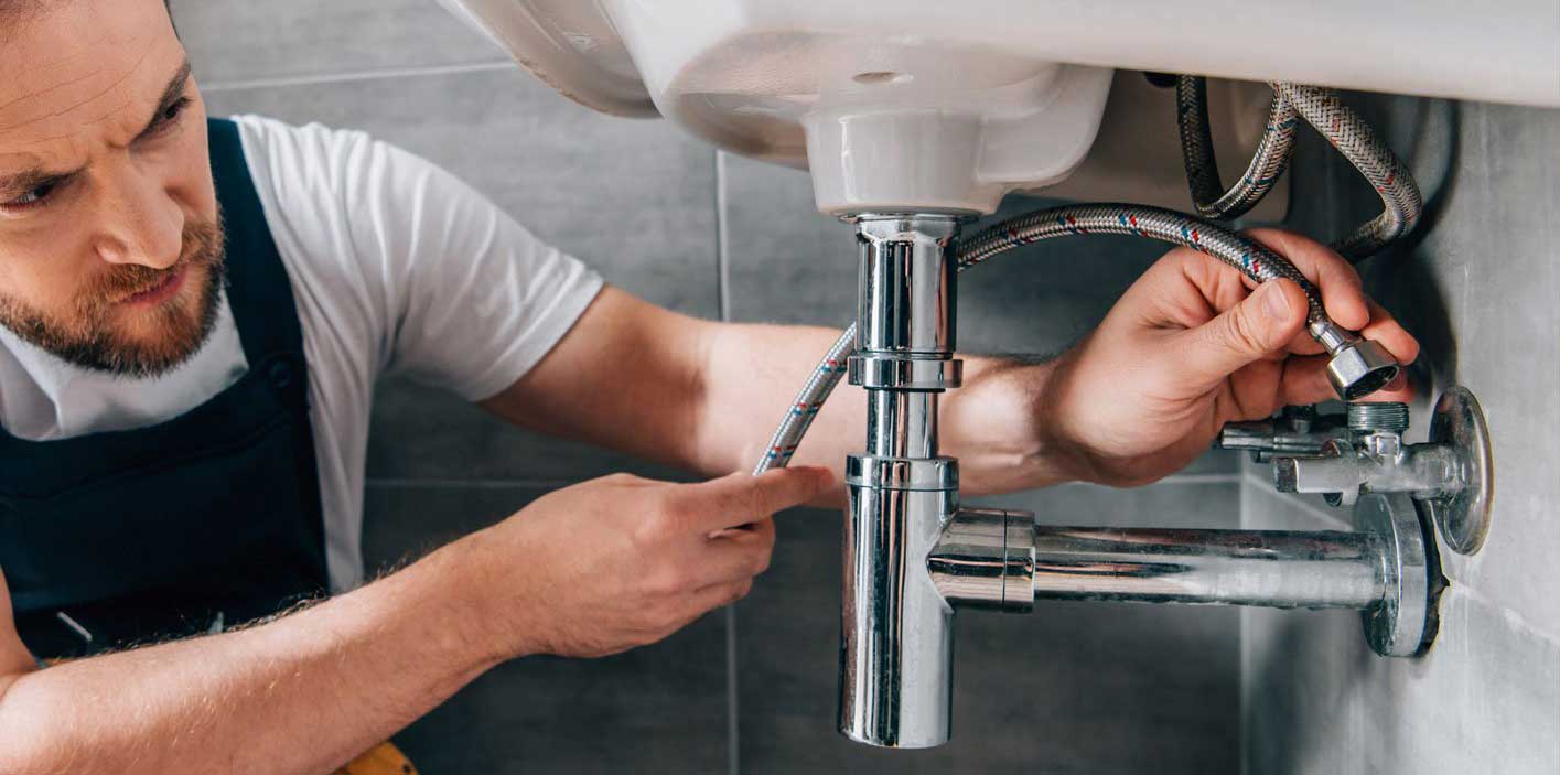 Plumber Attaching Water Pipes Plumber repairing sink plumbing with chrome pipes and flexible hoses, illustrating professional plumbing services offered by Edge Plumbing LLC in Arizona.