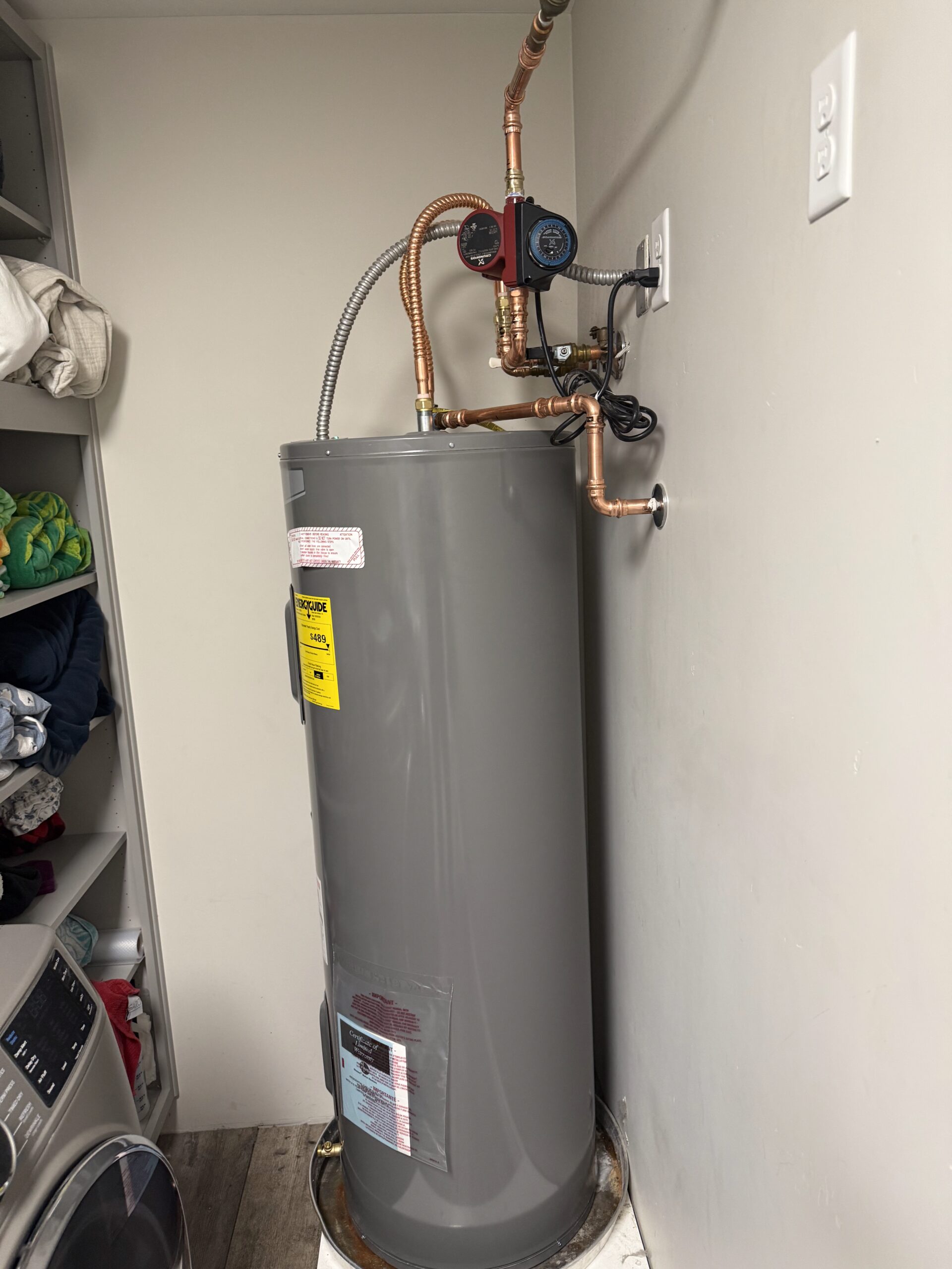 Water heater installation in a residential laundry area, featuring copper piping and gauges, highlighting Edge Plumbing's service for water heater replacements in Phoenix, AZ.