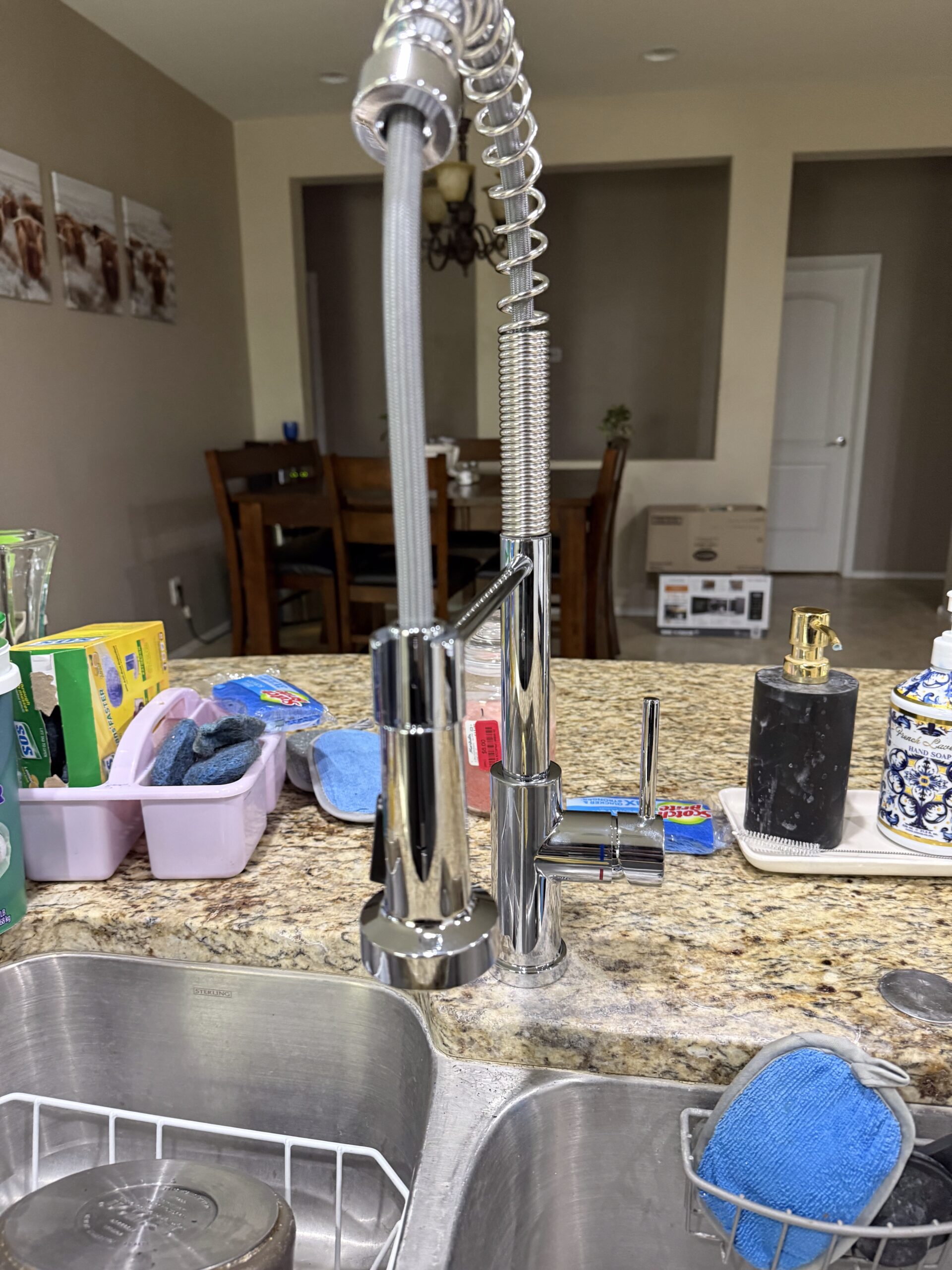 Kitchen sink with newly installed chrome faucet and sprayer, surrounded by cleaning supplies and dining area in background, illustrating Edge Plumbing's faucet replacement service in Peoria, AZ.