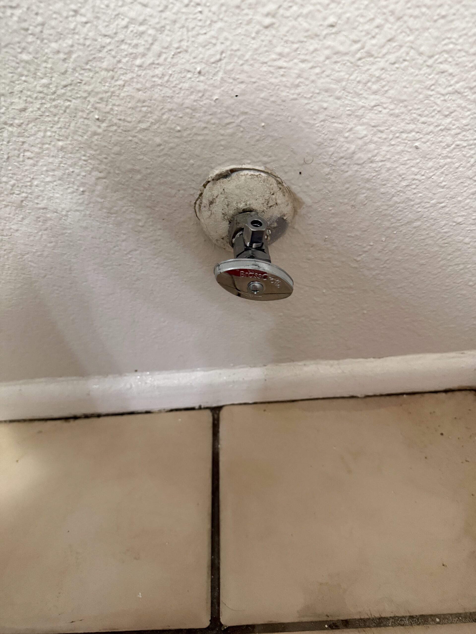 Close-up of a plumbing shut-off valve installed on a wall, near tiled flooring, relevant to emergency plumbing services offered by Edge Plumbing LLC in Glendale, AZ.