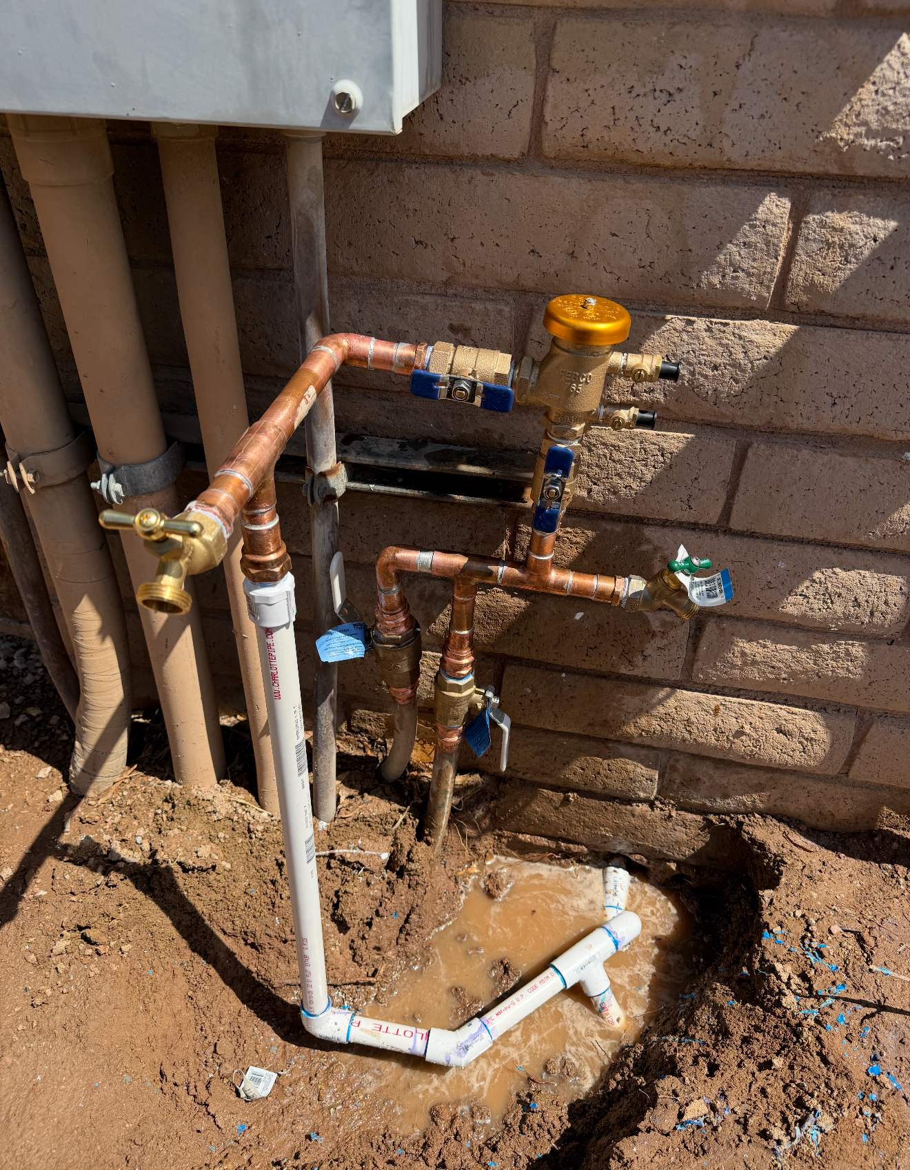 IMG_2458 Plumbing installation showing copper and PVC pipes, water meter, and muddy area with standing water, relevant to Edge Plumbing LLC's services in Gilbert, AZ.