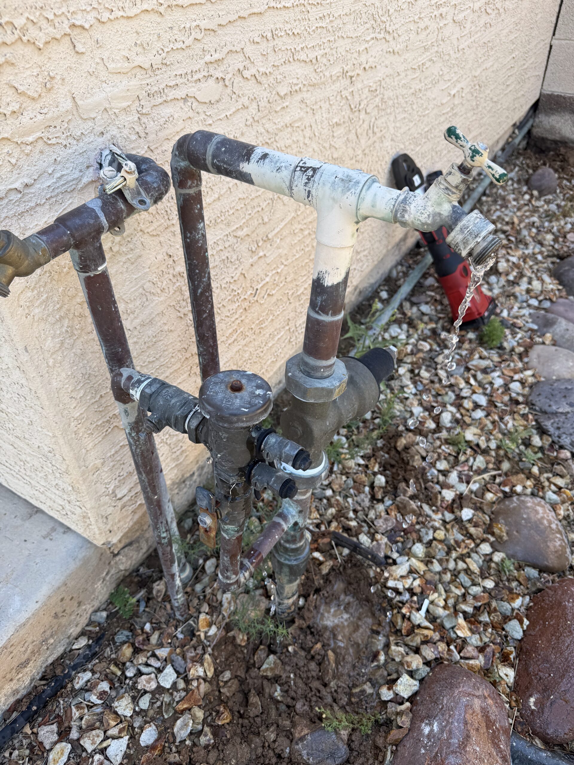 Leaking main water supply line with visible water flow, plumbing fixtures, and rocky landscape, relevant to Edge Plumbing's leak detection services in Phoenix, AZ.