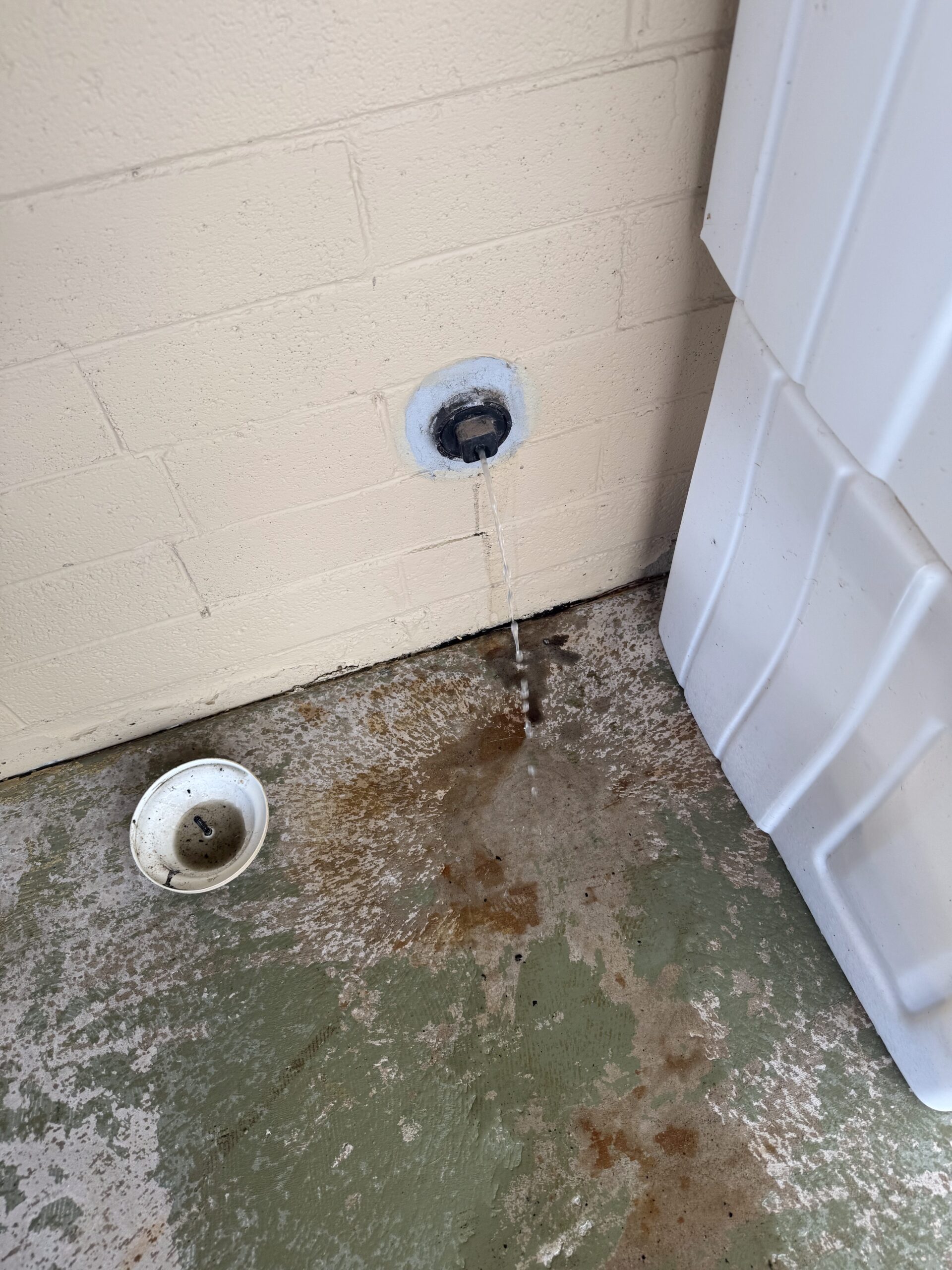 Water leaking from a drain pipe onto stained concrete floor, with a white basin nearby, illustrating plumbing issue addressed by Edge Plumbing in Phoenix, AZ.