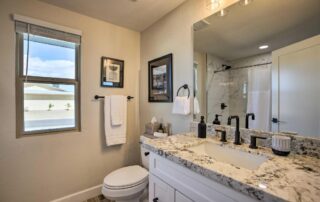 Modern bathroom featuring a granite countertop, white cabinetry, and a toilet, with natural light from a window, reflecting Edge Plumbing's expert installation services.