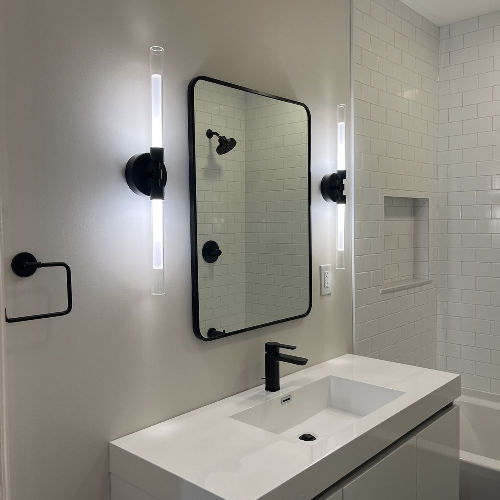 Modern bathroom vanity with sleek black fixtures, illuminated wall sconces, and a large mirror, showcasing a stylish remodel by Edge Plumbing LLC in Waddell, AZ.