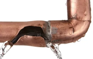 Copper pipe with a crack leaking water, illustrating plumbing issues related to cooler temperatures and burst pipes.