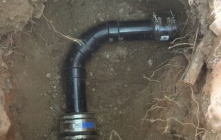 Sewer pipe installation in trench showing curved black piping and connectors, relevant to plumbing repair services in Surprise, AZ.