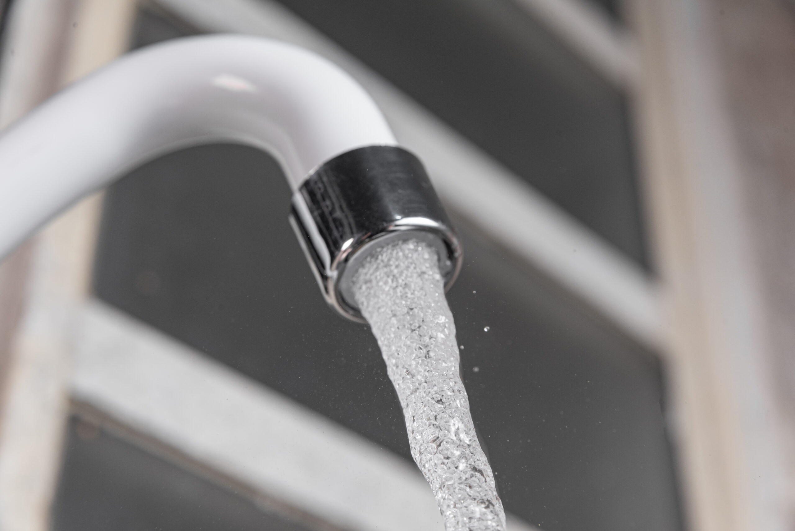 Close-up of a modern white kitchen sink faucet with flowing water, highlighting plumbing solutions relevant to Edge Plumbing's services in Surprise, AZ.